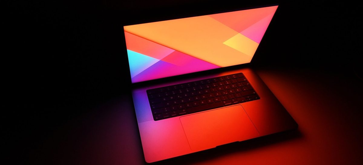 A MacBook Pro open in the dark, its screen glowing bright orange and pink