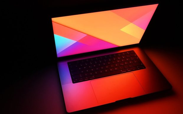 A MacBook Pro open in the dark, its screen glowing bright orange and pink